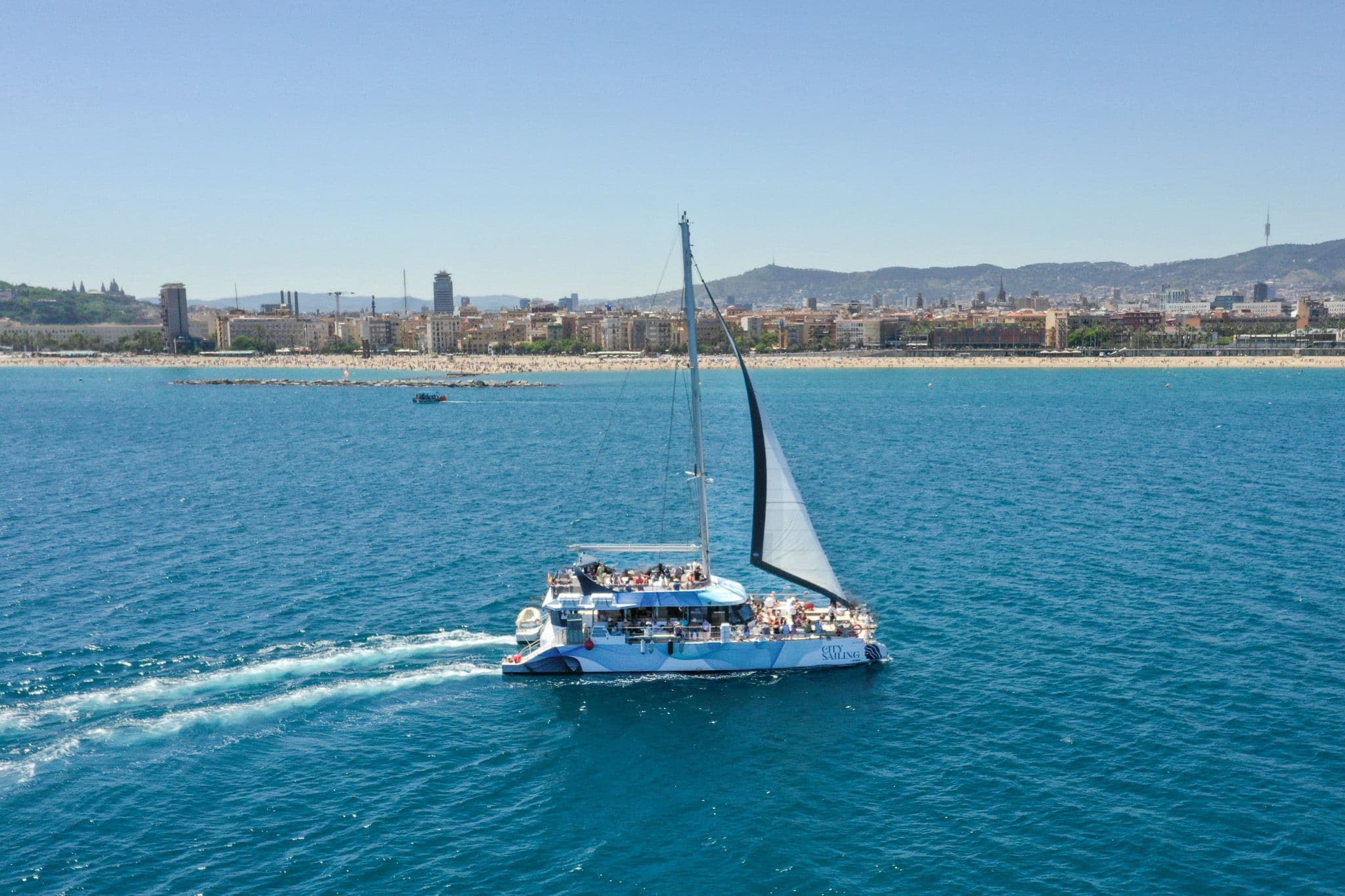 A large catamaran hosts a corporate sailing team event on the Mediterranean Sea off Barcelona.
