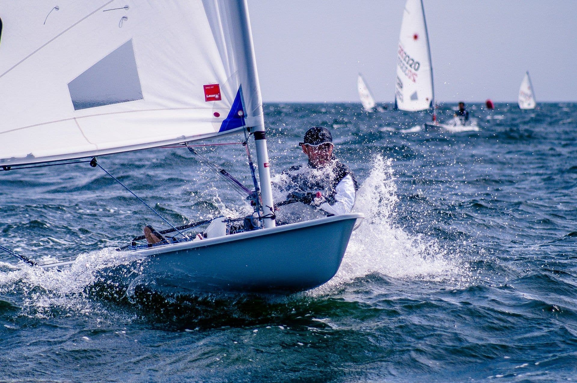 A person sails a small dinghy, creating splashes, during an outdoor team building activity.