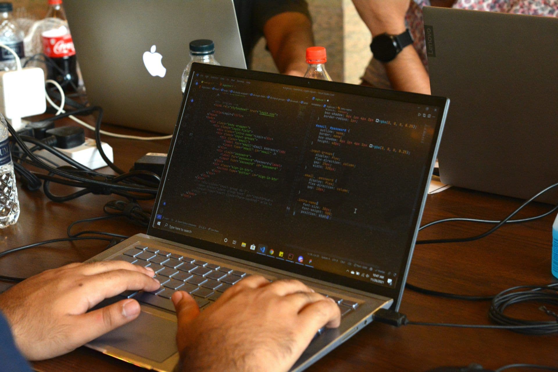 Hands coding on a laptop during a corporate workshop, with other laptops and refreshments on a wooden table.