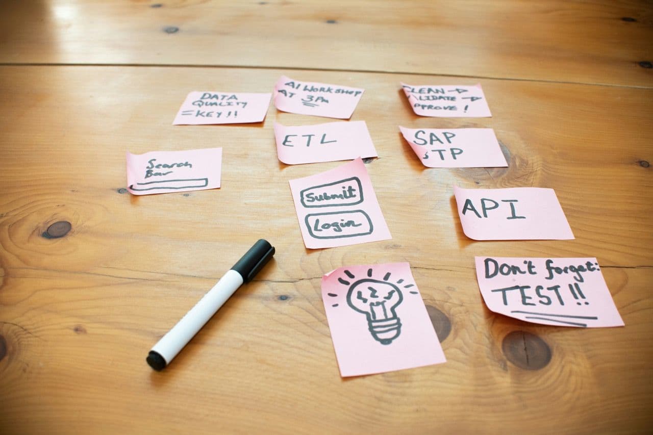 Pink sticky notes with project ideas and a marker on a wooden table, suggesting a corporate workshop.