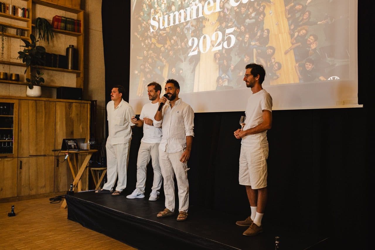 Four men present on stage at a corporate kickoff event, with "Summer 2025" displayed on a large screen.