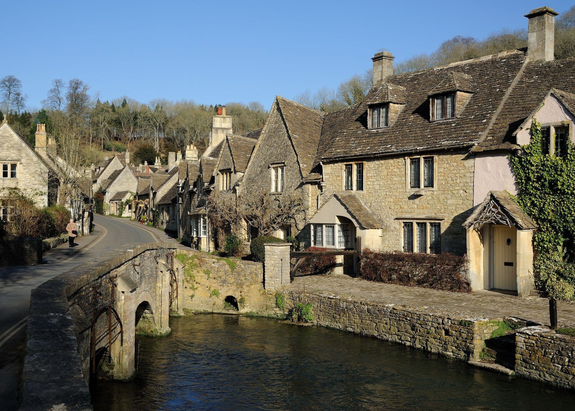 Historic stone cottages and a bridge over a river in Castle Combe, a unique Cotswolds venue.