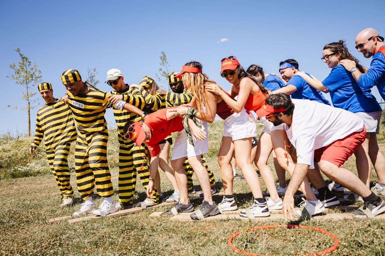 Colleagues in themed costumes participate in an outdoor team-building activity on a sunny day.