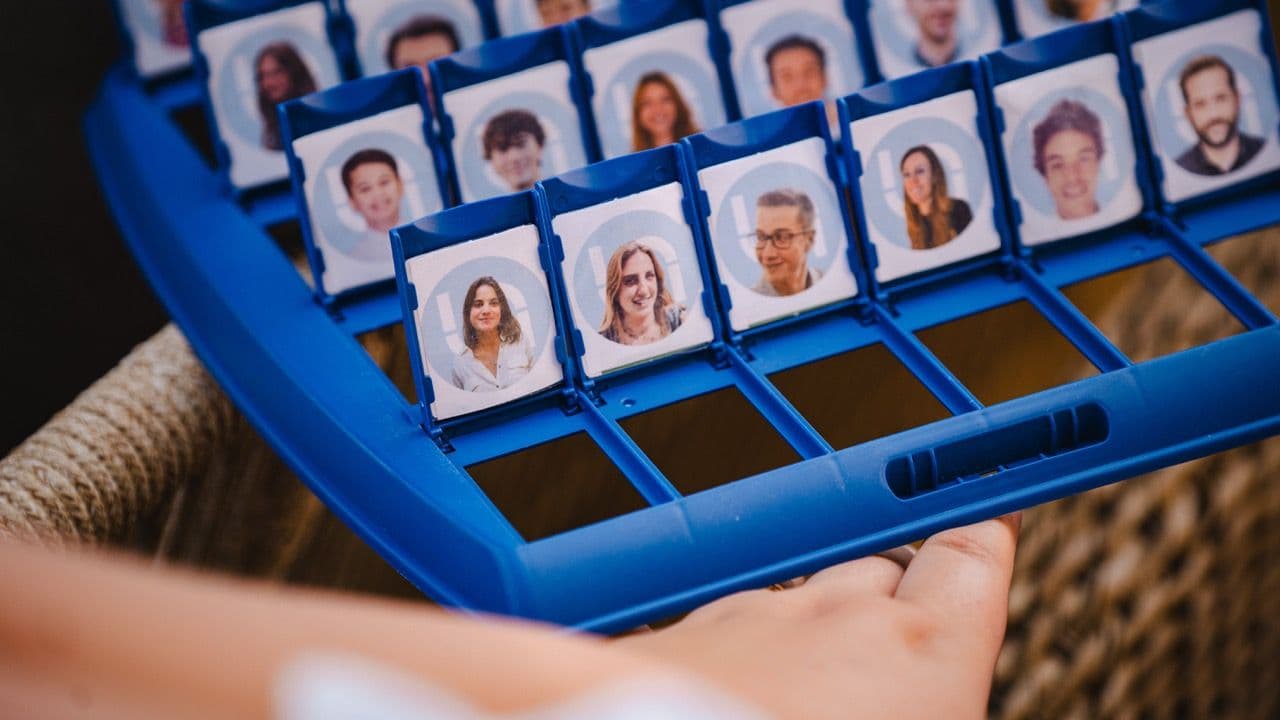 A close-up of a blue board game, similar to Guess Who, featuring photos of colleagues for a team building