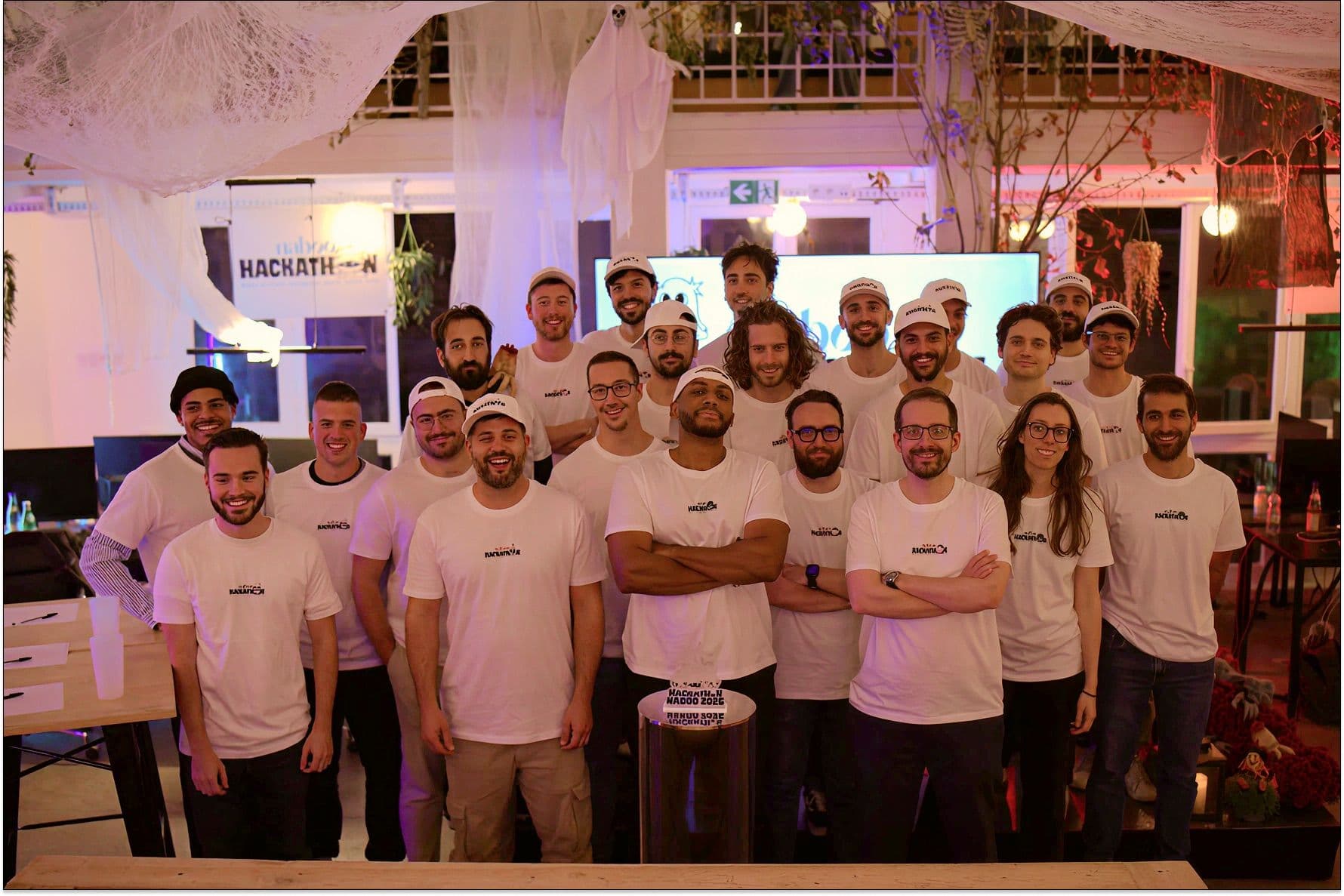 Smiling employees in branded t-shirts gather at a Naboo Hackathon in a festive corporate event venue.