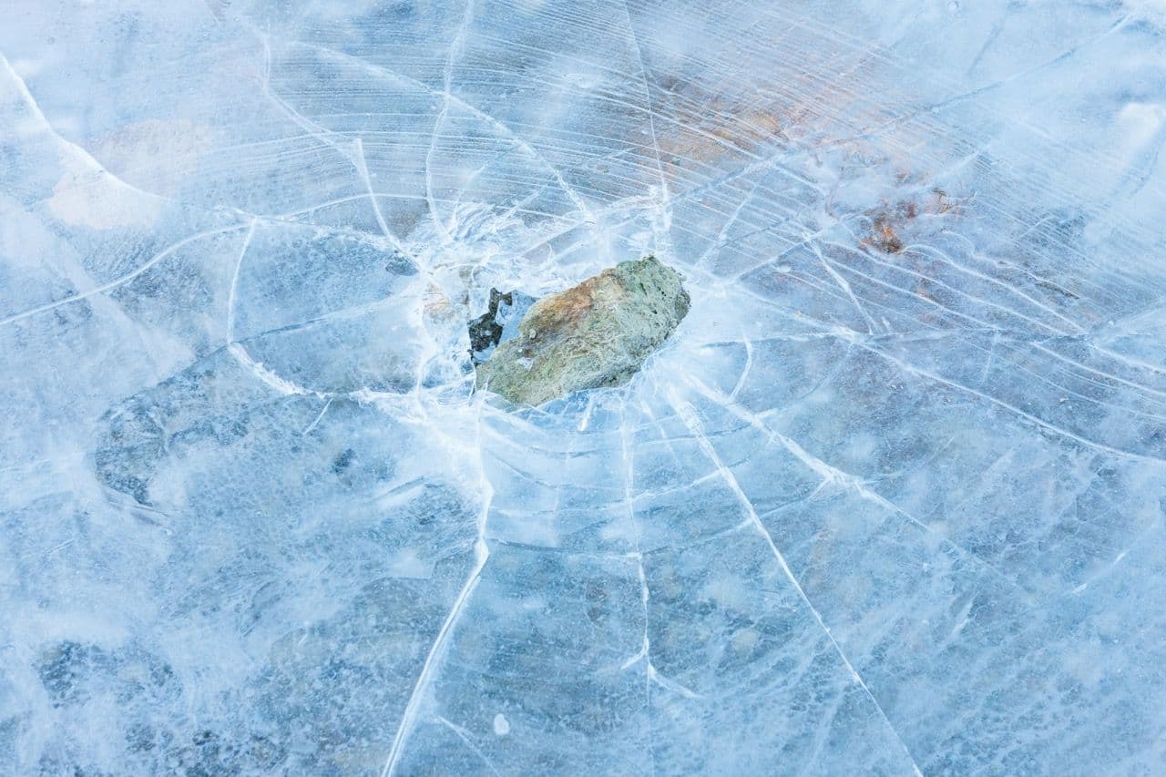 A rock has broken through a sheet of ice, creating radial cracks
