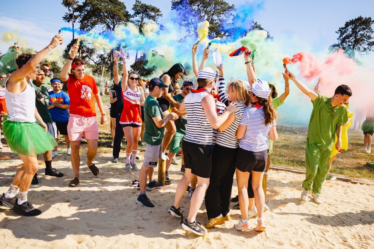Energetic group enjoying an outdoor team building activity with colorful smoke flares and costumes.