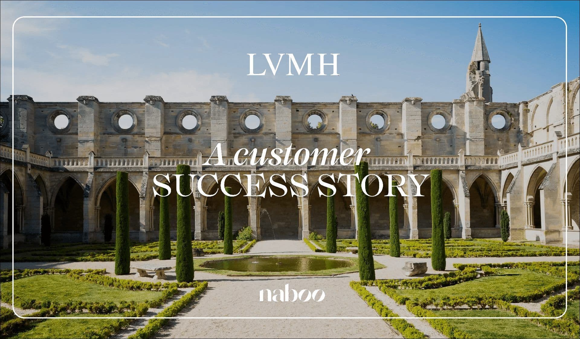 A historic stone building with arched cloisters and a spire surrounds a formal garden with cypress trees and