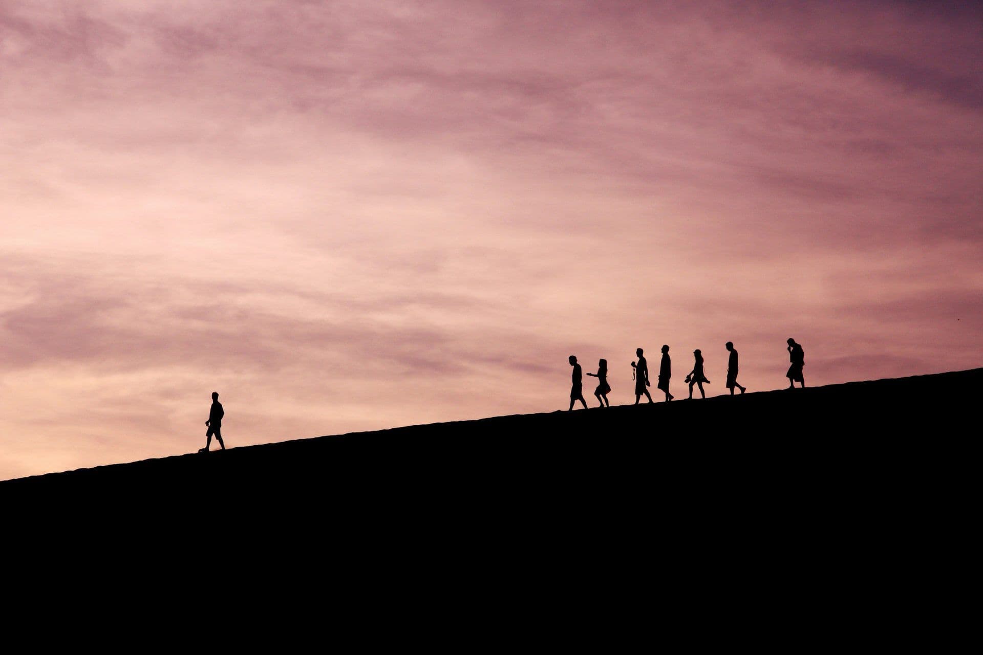 Silhouettes of a team walking up a desert dune at sunset, perfect for an outdoor team building activity.