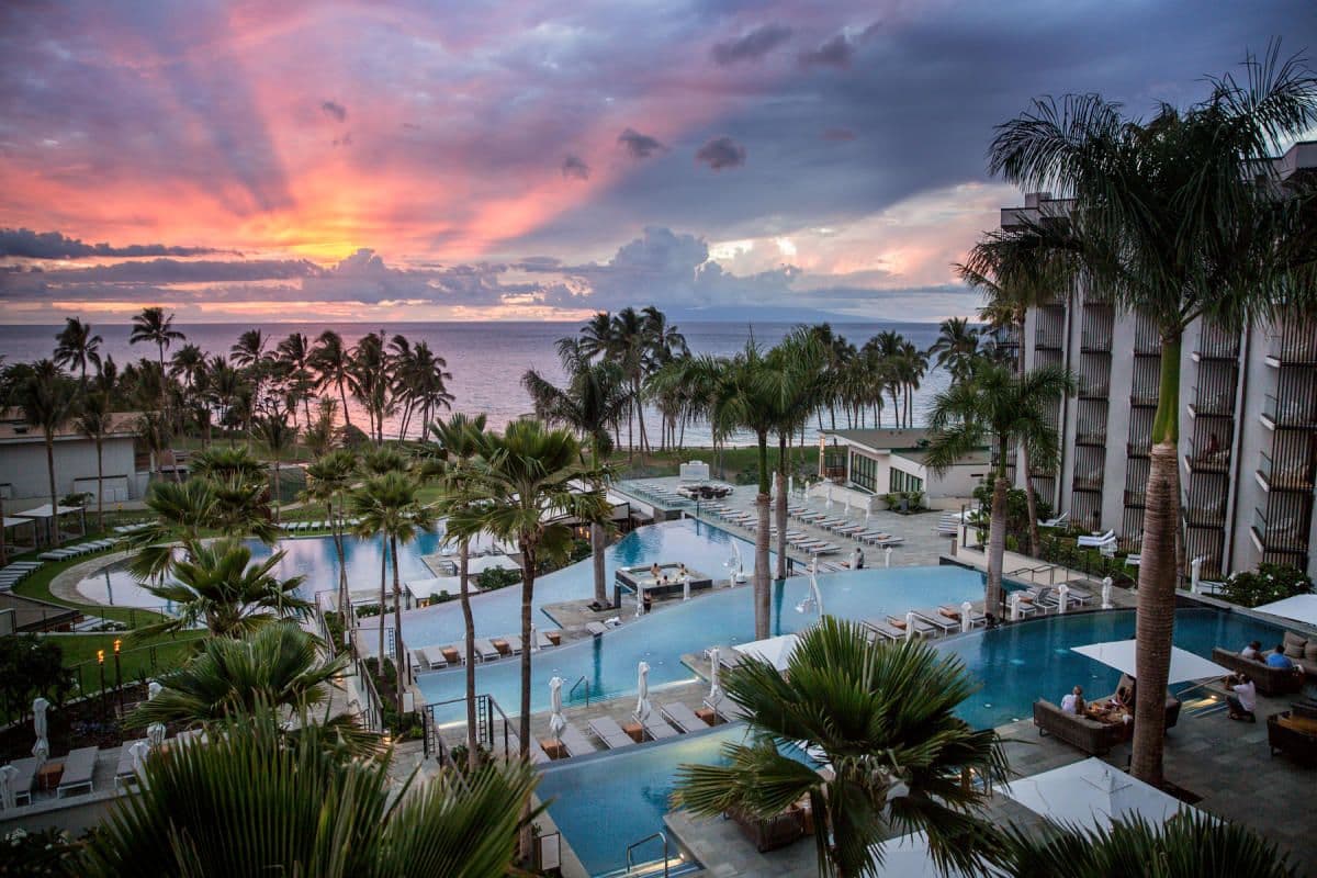 Waterfront resort with tiered pools, palm trees, and a vibrant sunset, ideal for corporate retreats.