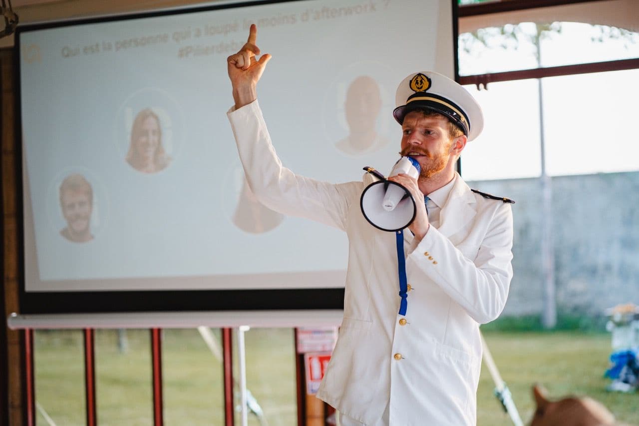 A man in a captain's uniform leads an interactive corporate team building quiz with a megaphone.
