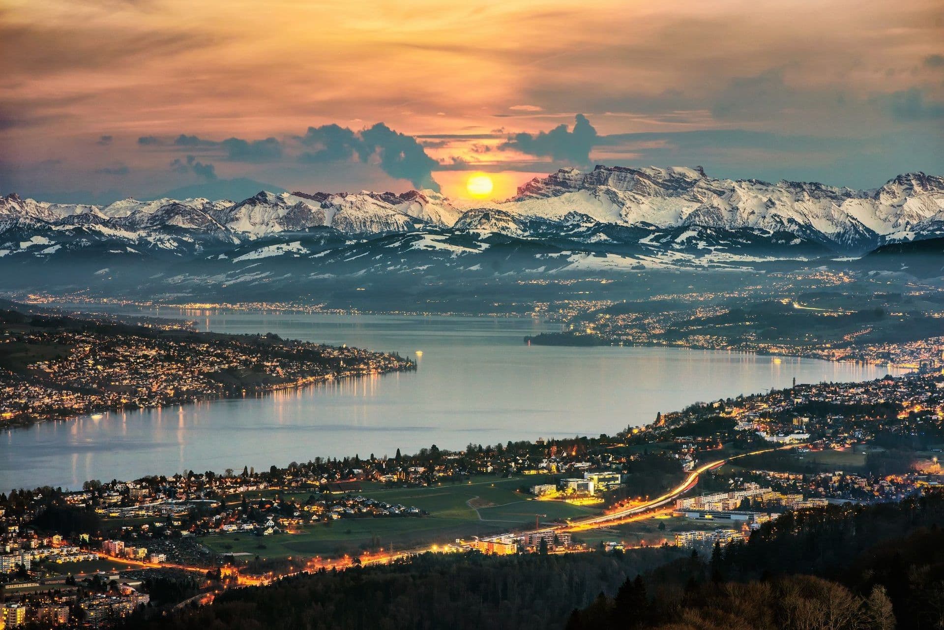 Panoramic sunset view of Lake Zurich and the city with snow-capped Alps, ideal for a corporate retreat.