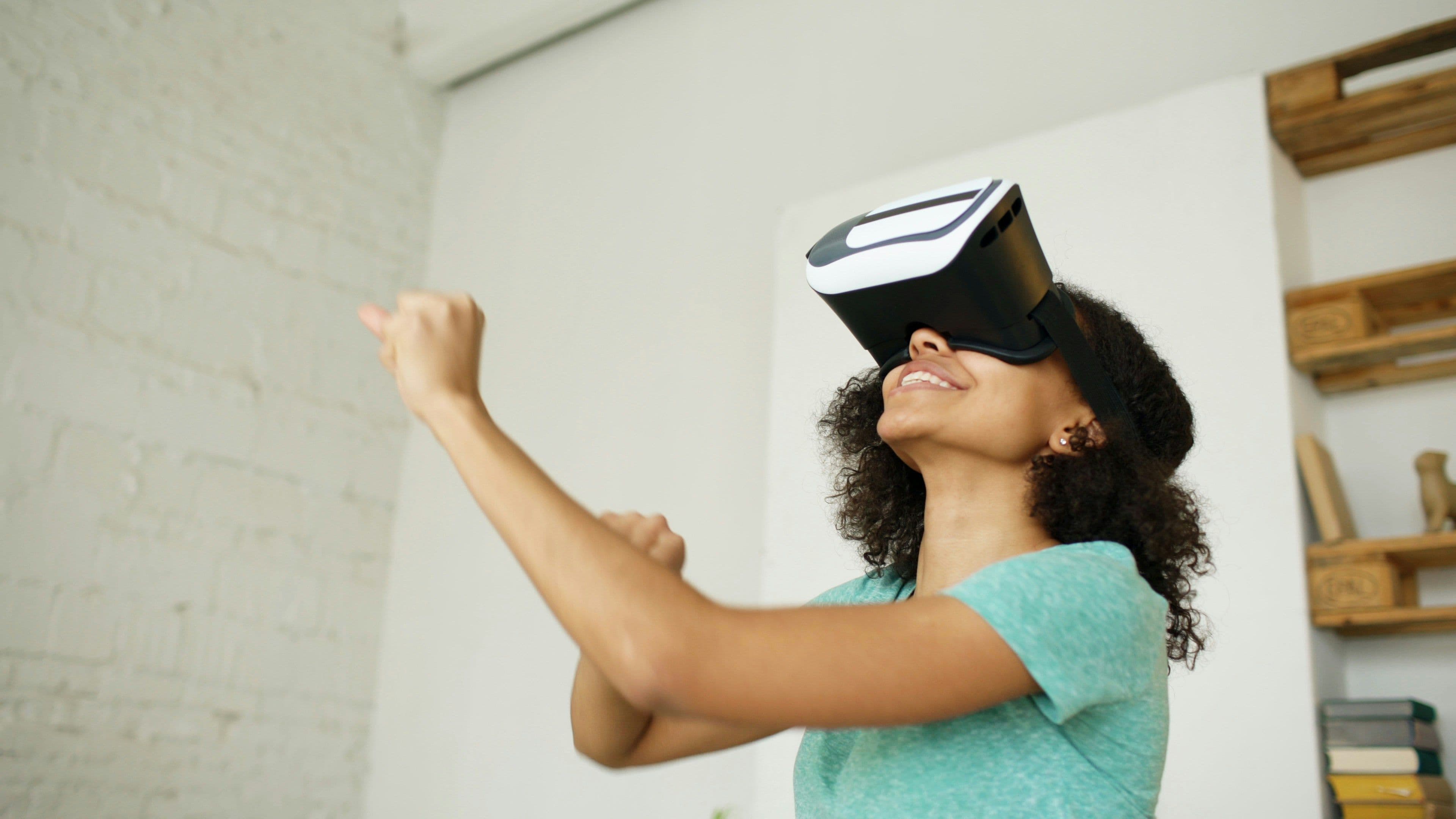 A smiling woman with curly hair wears a VR headset, engaging in a virtual reality team building activity.
