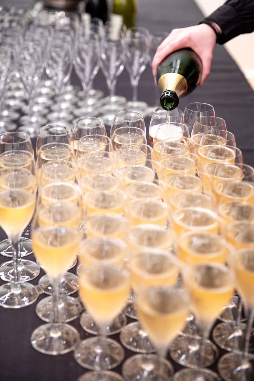 A hand pours champagne into many glasses on a black table, ready for a corporate cocktail reception.