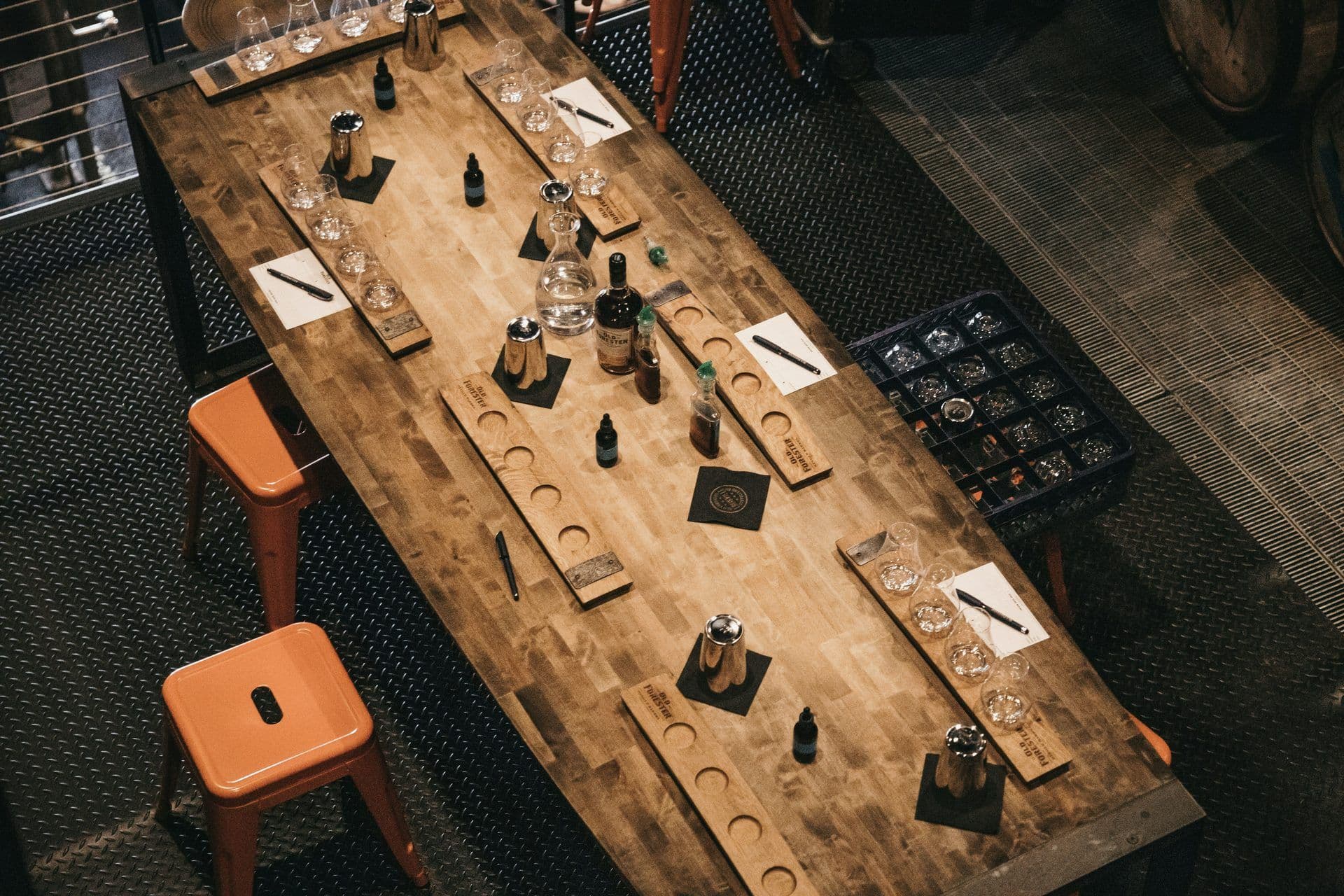 Overhead view of a long wooden table set for a spirit tasting event with glasses, bottles