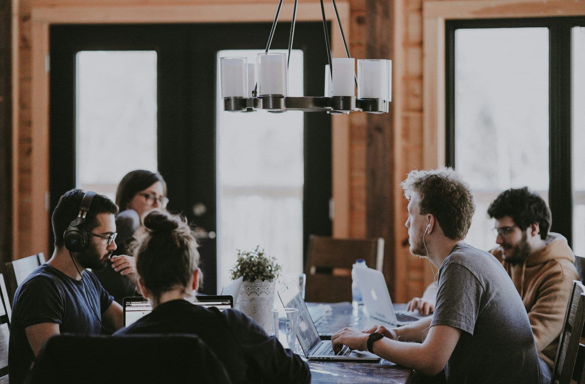Employees collaborate on laptops at a wooden table in a well-lit meeting room, ideal for a corporate workshop.