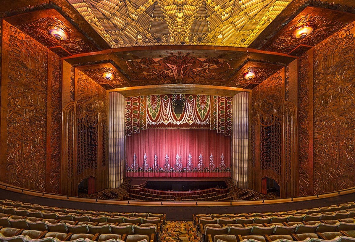 Grand historic auditorium with an ornate ceiling, red stage curtain