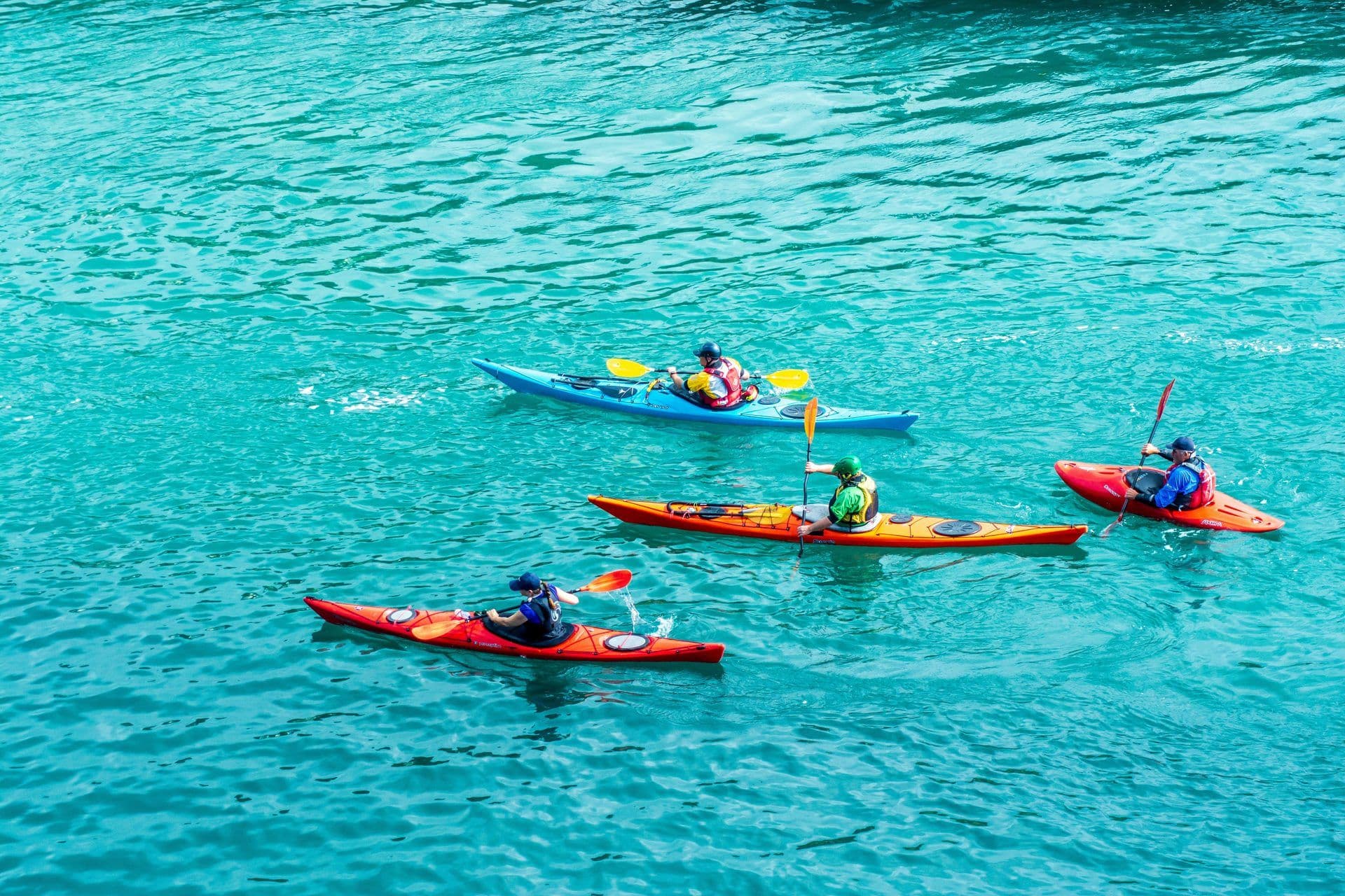 Four people in colorful kayaks paddle on bright turquoise water, ideal for an outdoor team building activity.