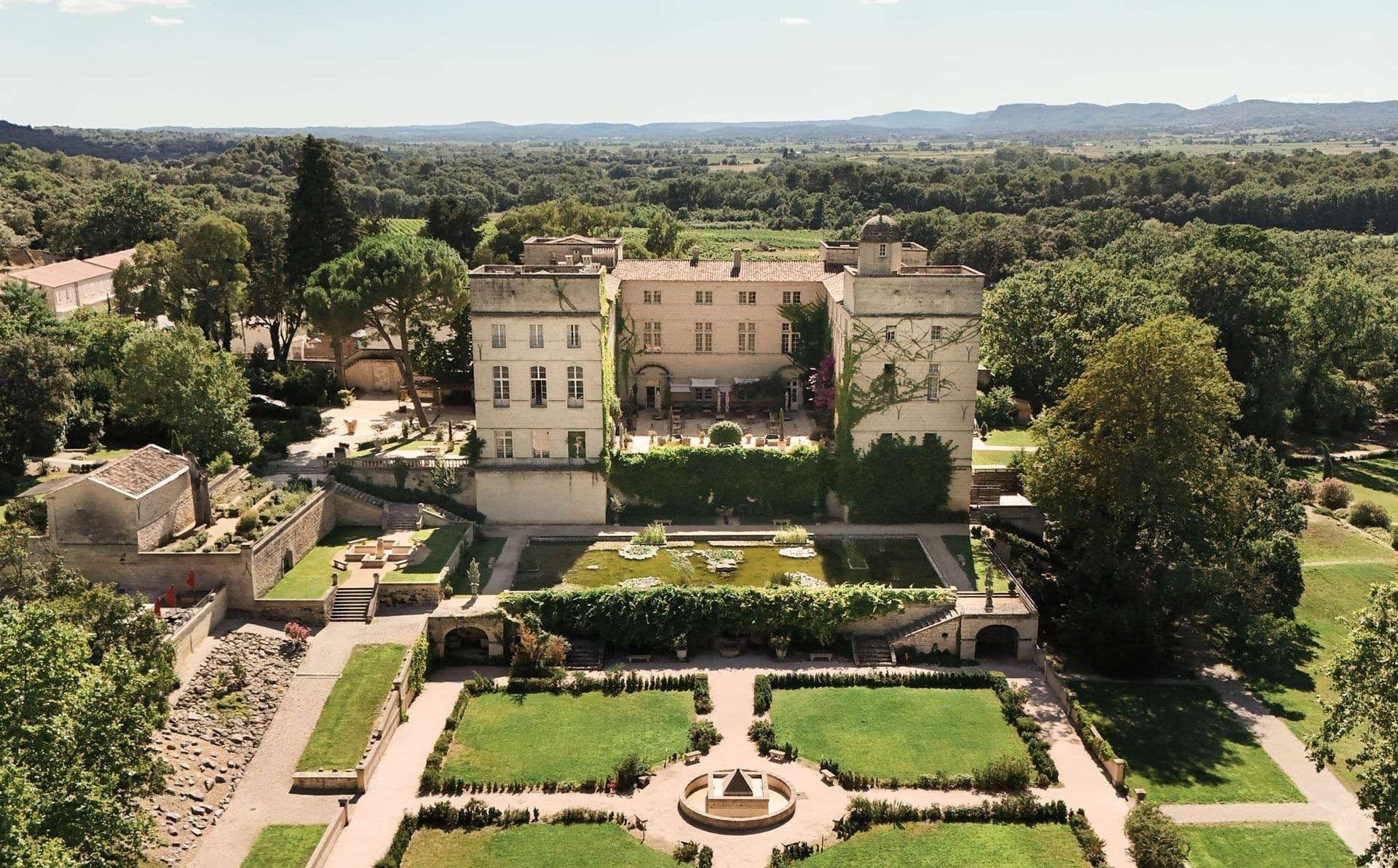 Aerial view of a grand historic French estate with formal gardens, a pond, and vineyards
