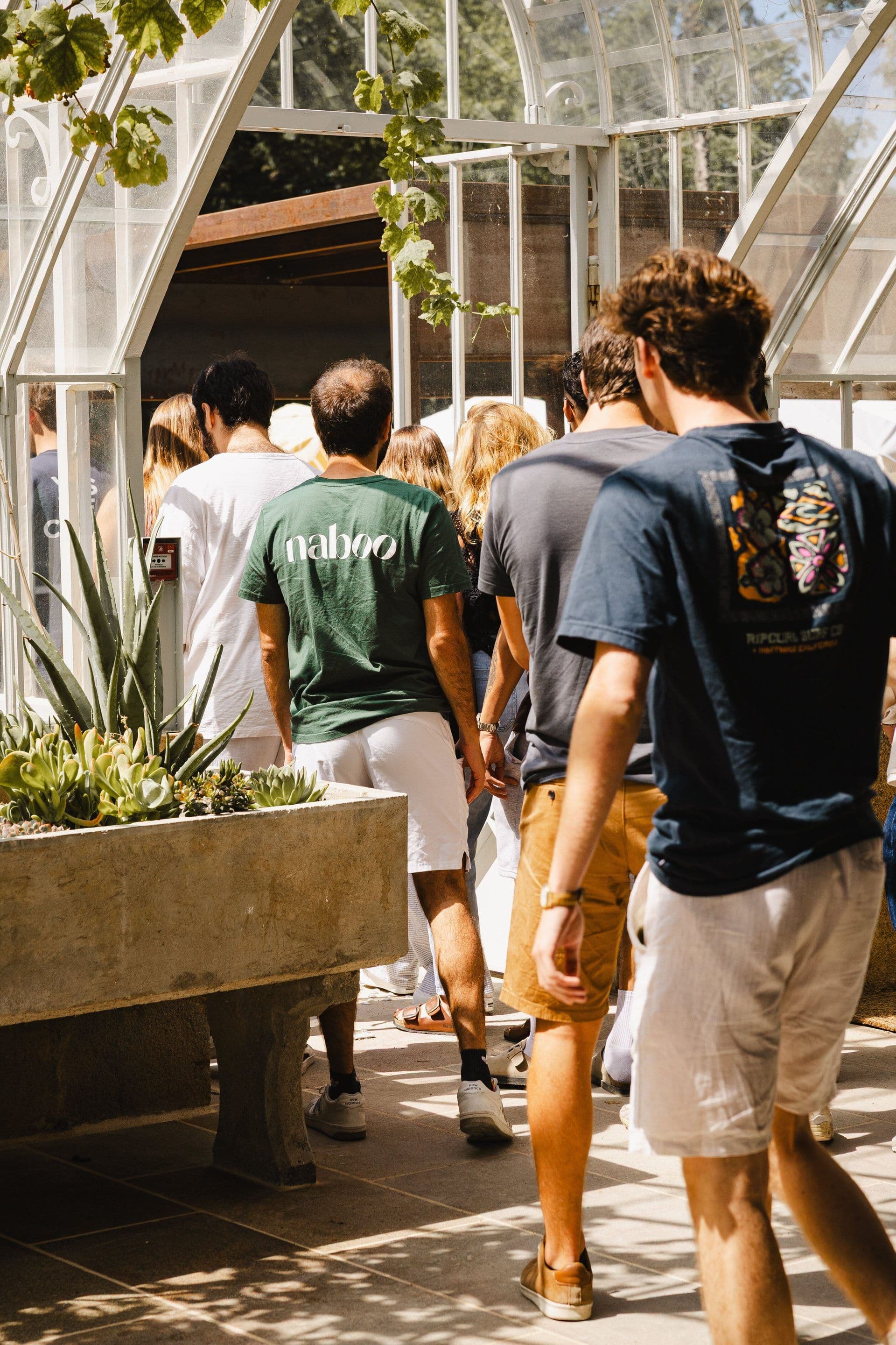 A group of colleagues, one in a Naboo t-shirt, entering a sunny glasshouse venue for a corporate event.