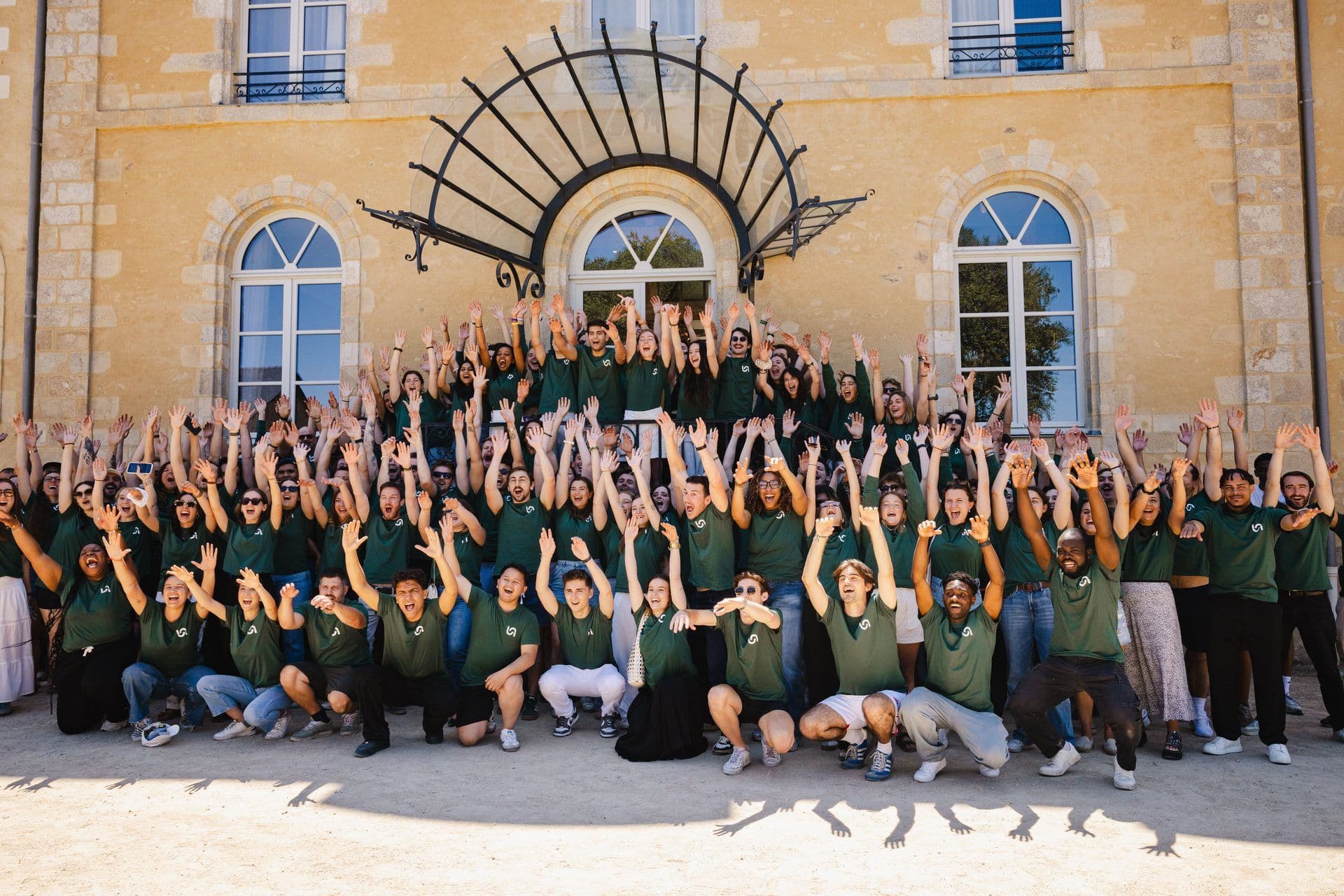 Excited employees in green shirts celebrating outdoors during a corporate team offsite at a historic venue.