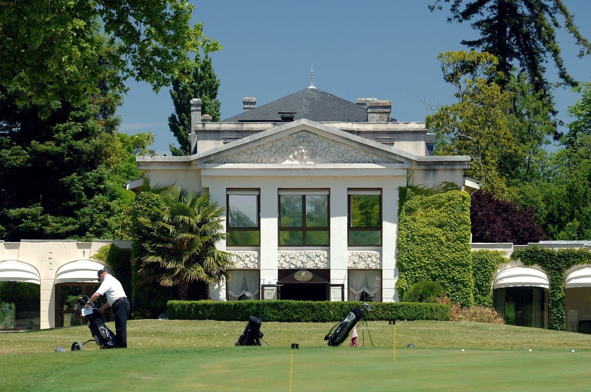 Elegant corporate event venue and golf course with a classical facade, a golfer, and golf bags in Margaux