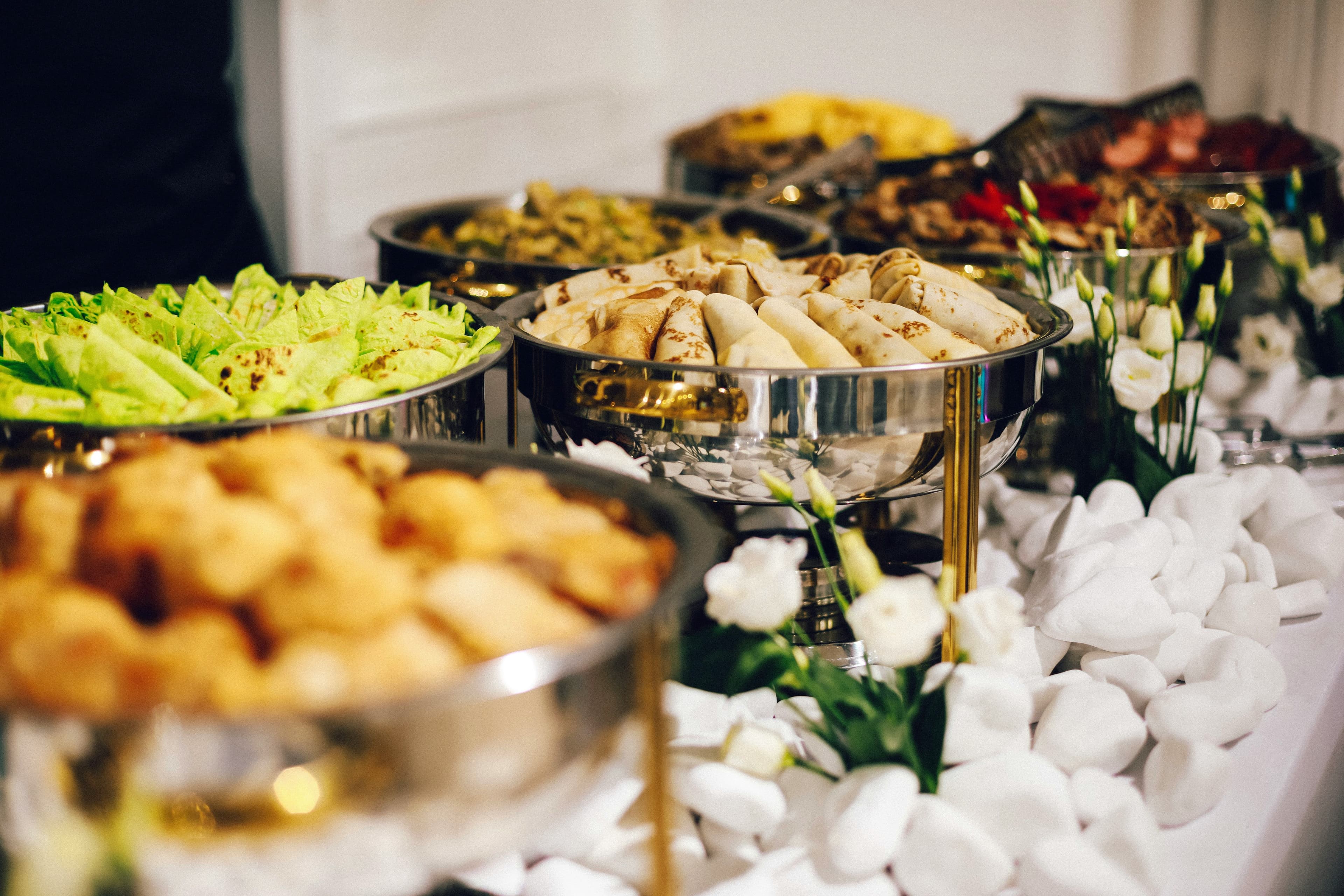 An elegant event catering buffet with silver chafing dishes, canapes and white floral decoration