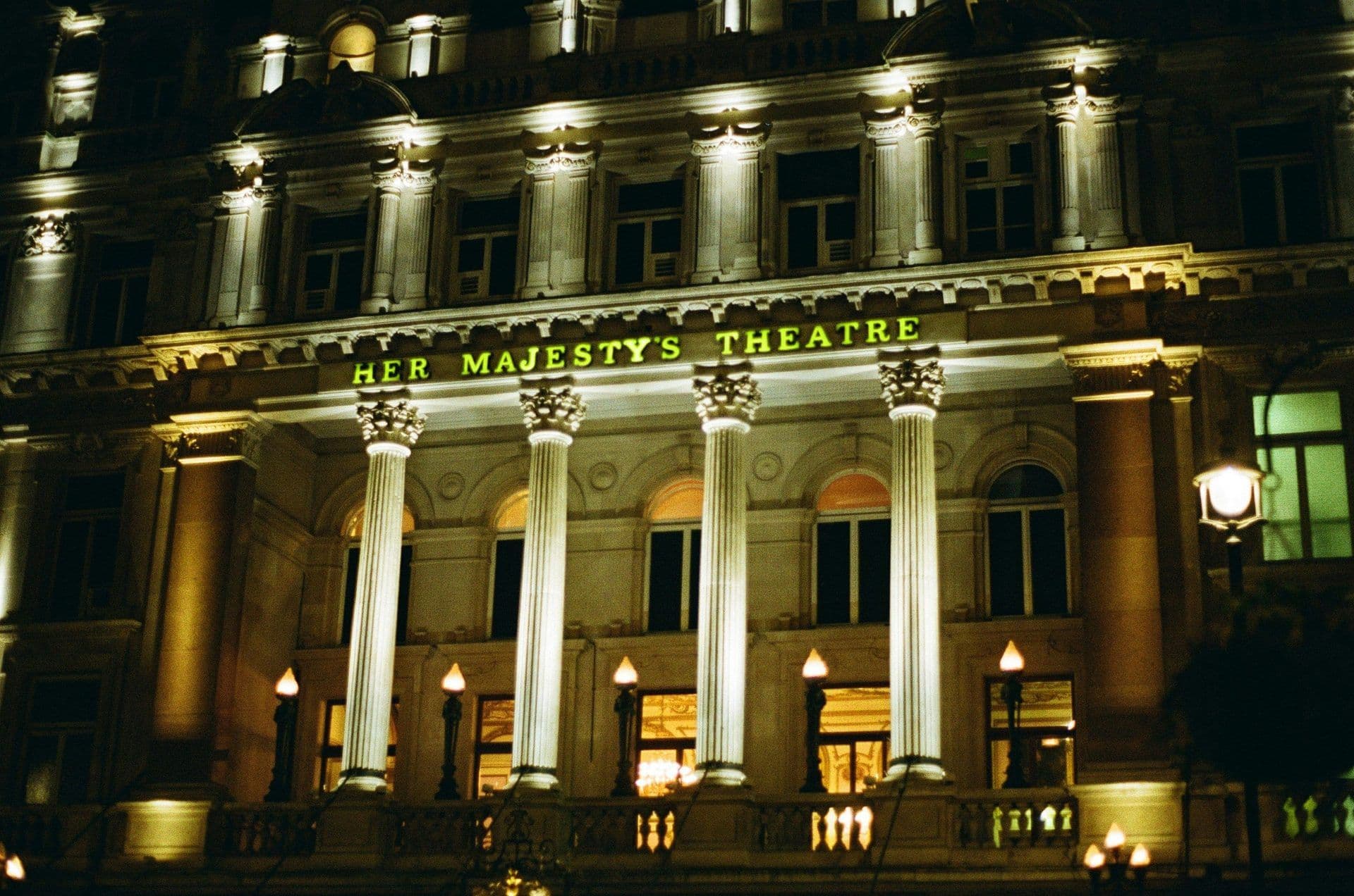 Her Majesty's Theatre, a grand historic venue in London, illuminated at night with classical columns.