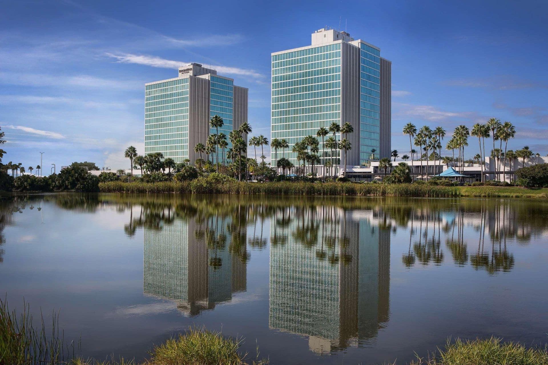Two DoubleTree by Hilton hotel towers and palm trees reflected in a lake, ideal for corporate events.