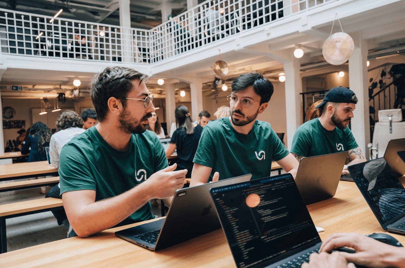 Team members collaborate on laptops during a workshop in a bright, multi-level corporate event venue.