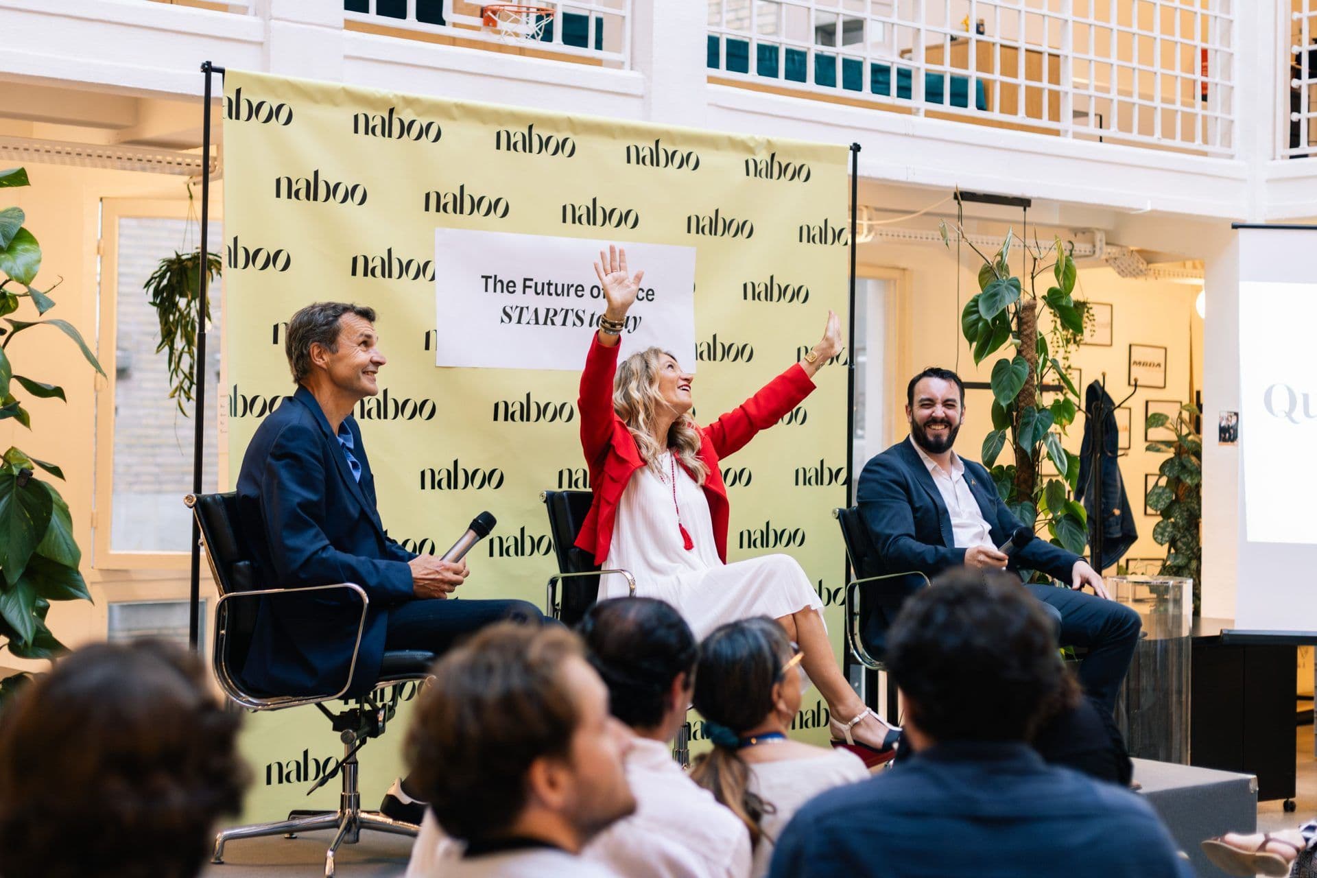 Three speakers lead a lively panel discussion at a corporate seminar in a modern event venue.