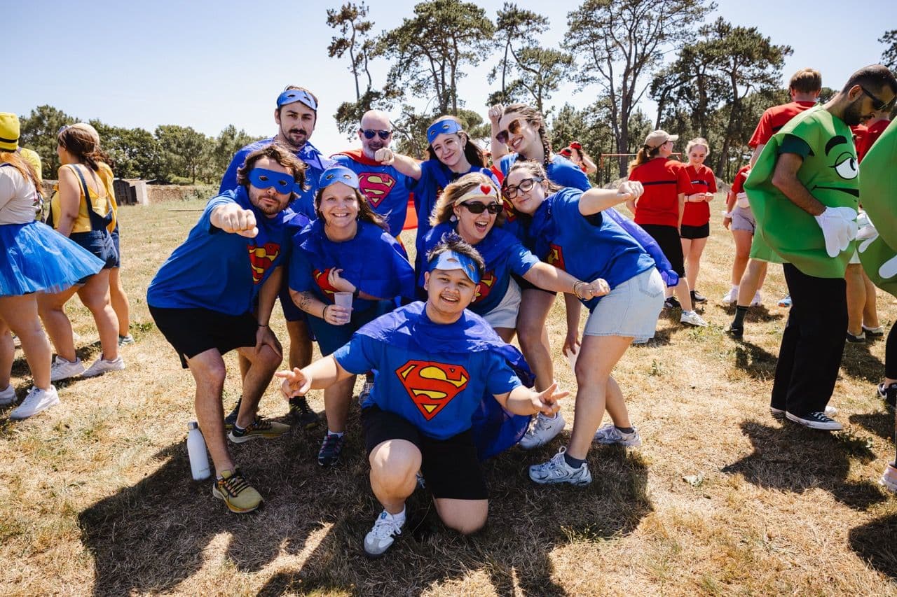 Employees in Superman costumes pose outdoors during a fun team building event or company away day.