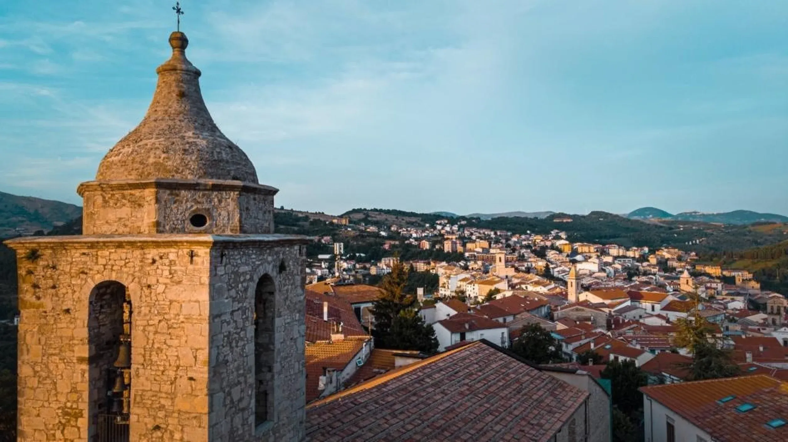 Historic stone bell tower overlooking the charming town of Isernia, Italy, surrounded by hills.
