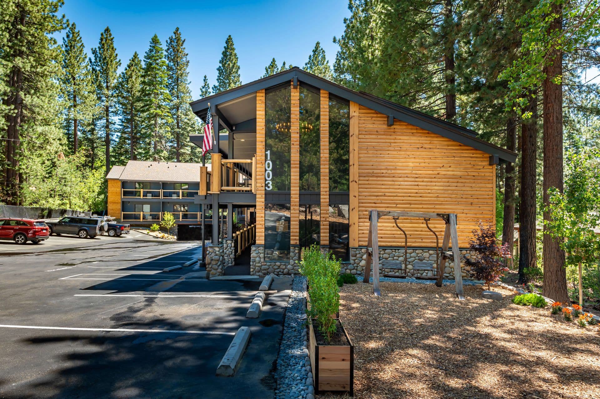 Modern wood and glass corporate retreat venue with a US flag, nestled among tall pine trees.