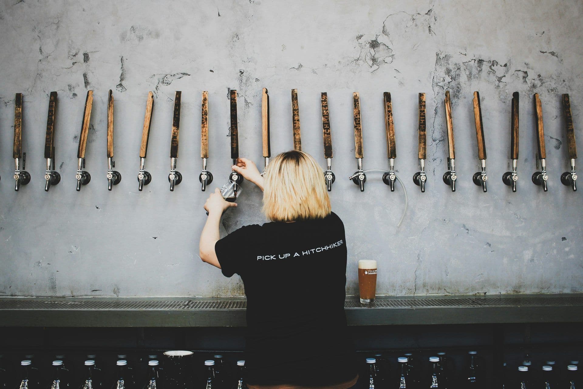 A person pours beer from one of many taps with wooden handles at a modern brewery venue.