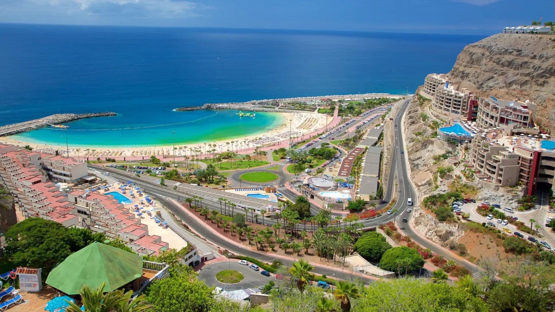 Panoramic view of a beach, turquoise ocean, and cliffside corporate event venues in Gran Canaria, Spain.