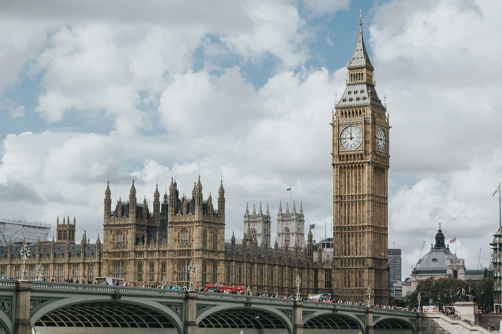 Big Ben and the Houses of Parliament in London, with Westminster Bridge bustling with people and traffic.