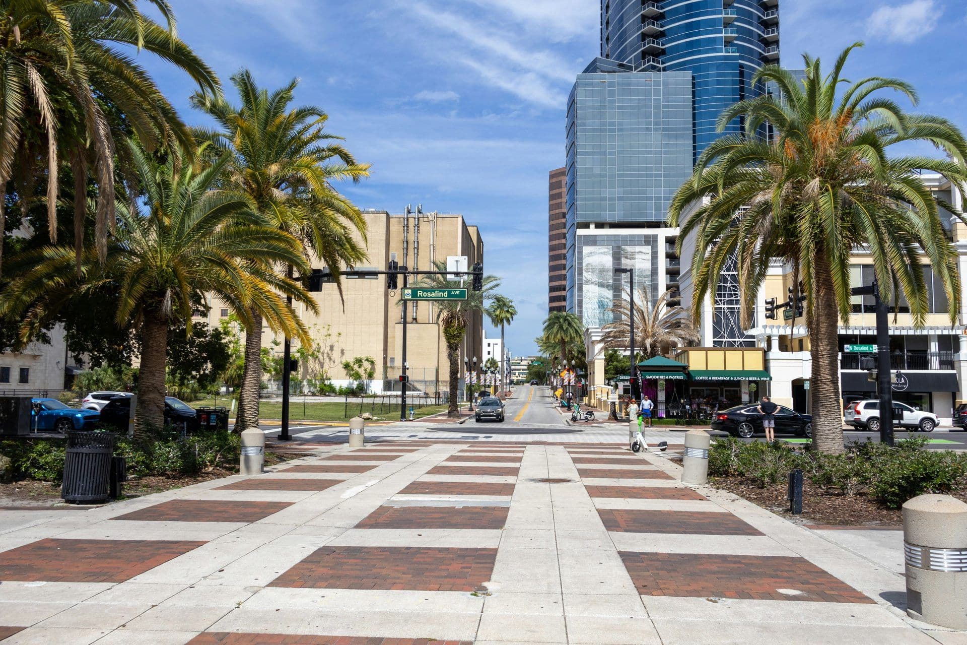 A sunny street scene in Orlando, Florida, with palm trees, modern buildings, and a patterned sidewalk.