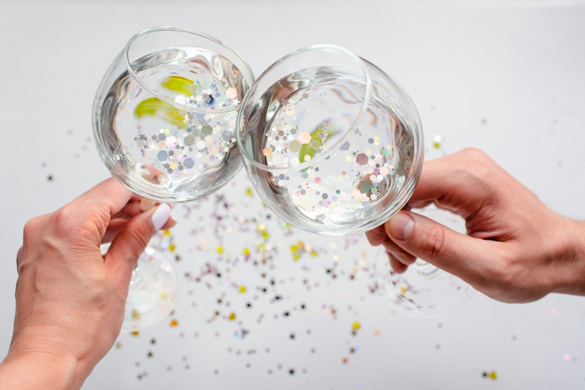 Hands holding wine glasses amid sparkling confetti at a Silvester office party