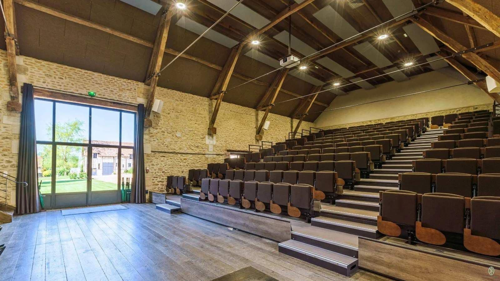 A spacious auditorium in a historic corporate event venue with tiered seating, a stage, stone walls