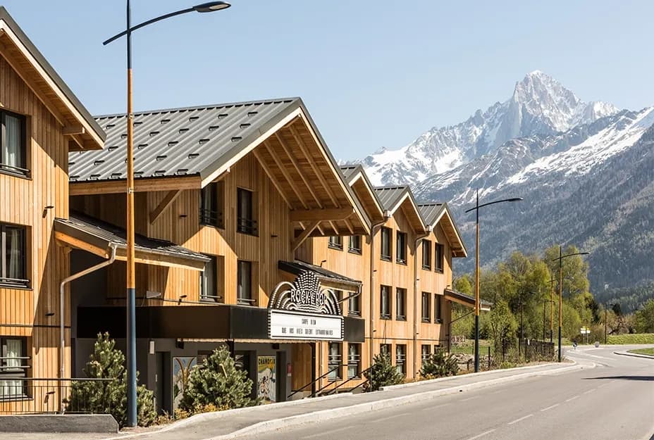 Modern wooden mountain resort building with a 'ROCKYPOP' sign and snow-capped peaks in Chamonix, France.