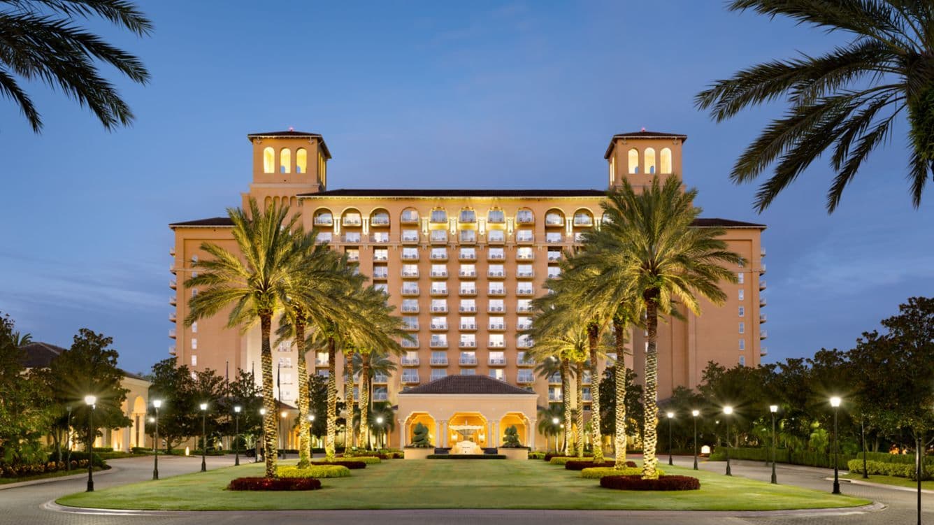 Grand luxury hotel exterior at dusk with illuminated palm trees, perfect for corporate events in Orlando