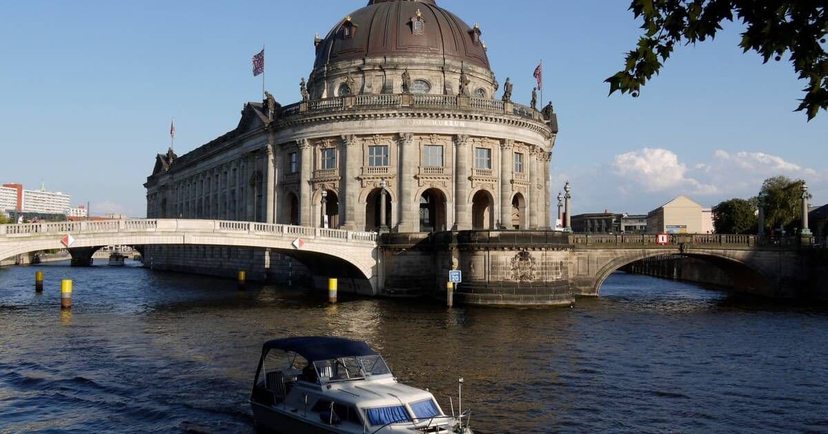 Historic waterfront venue in Berlin with a boat on the Spree River under a blue sky.
