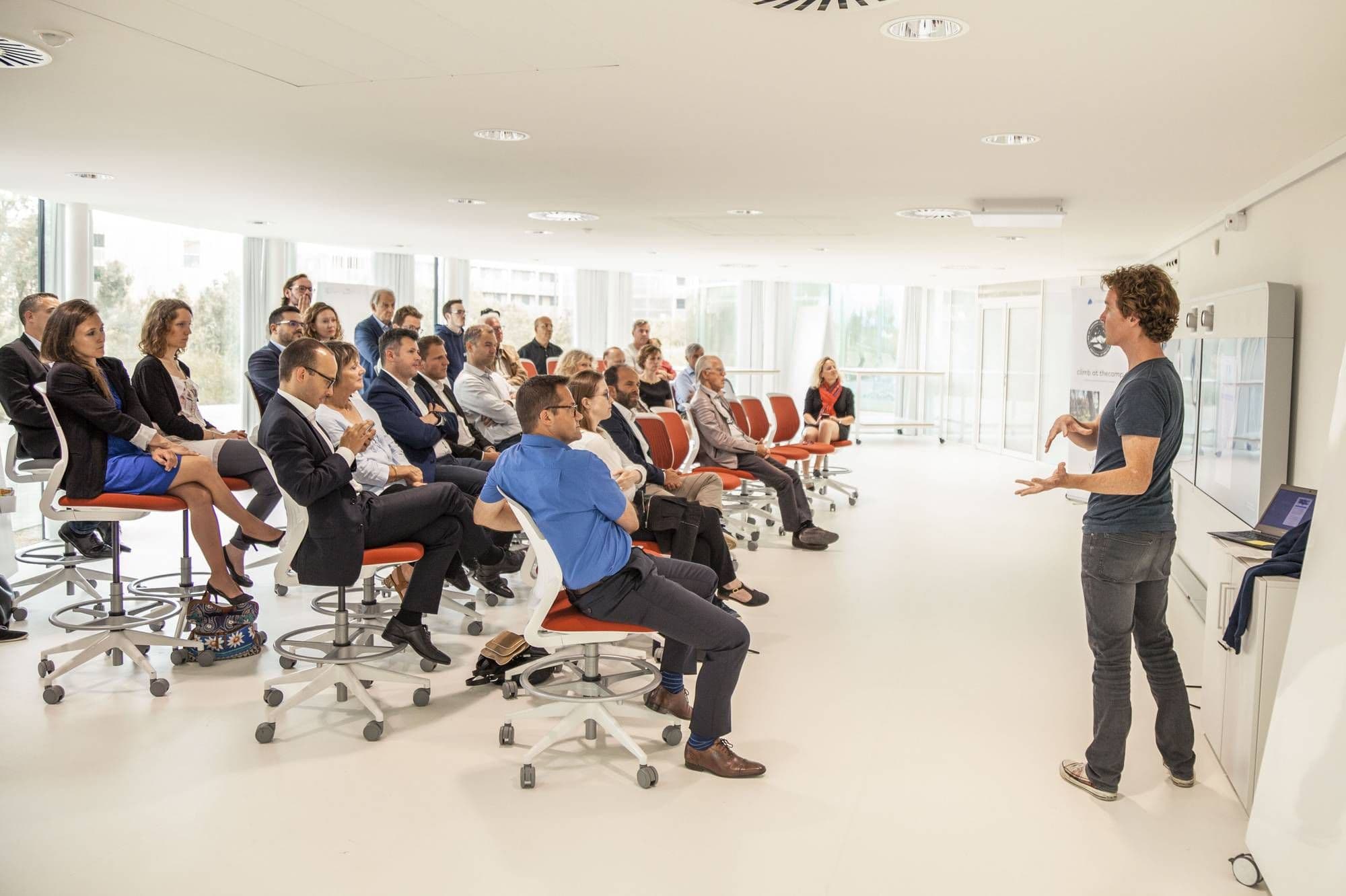 Professionals attend a corporate seminar in a bright, modern conference space with a speaker.