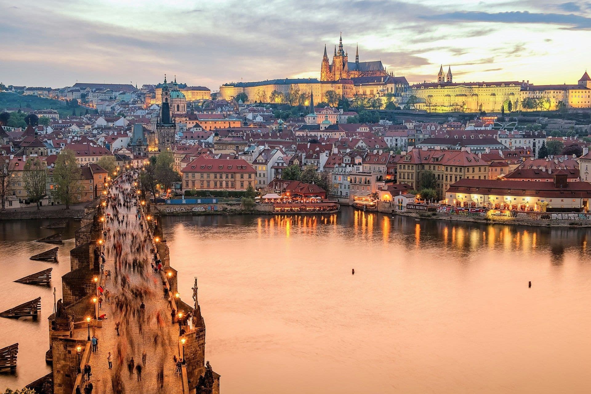 Historic Prague cityscape at sunset, with Charles Bridge bustling and Prague Castle illuminated.